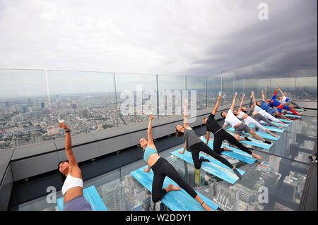 Bangkok, Tailandia. 7 Luglio, 2019. Gli appassionati di Yoga frequentare il vino sunrise yoga classe presso la terrazza sul tetto di Mahanakhon skywalk a Bangkok, Thailandia, Luglio 7, 2019. Vino di sunrise yoga unisce la gioia di bere il vino con lo yoga tradizionale pone mentre il bilanciamento delle bevande, sorseggiando e tostatura. Credito: Rachen Sageamsak/Xinhua/Alamy Live News Foto Stock