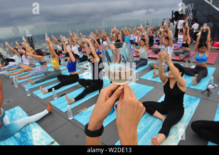 Bangkok, Tailandia. 7 Luglio, 2019. Gli appassionati di Yoga frequentare il vino sunrise yoga classe presso la terrazza sul tetto di Mahanakhon skywalk a Bangkok, Thailandia, Luglio 7, 2019. Vino di sunrise yoga unisce la gioia di bere il vino con lo yoga tradizionale pone mentre il bilanciamento delle bevande, sorseggiando e tostatura. Credito: Rachen Sageamsak/Xinhua/Alamy Live News Foto Stock