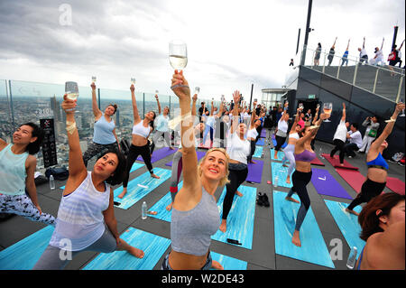 Bangkok, Tailandia. 7 Luglio, 2019. Gli appassionati di Yoga frequentare il vino sunrise yoga classe presso la terrazza sul tetto di Mahanakhon skywalk a Bangkok, Thailandia, Luglio 7, 2019. Vino di sunrise yoga unisce la gioia di bere il vino con lo yoga tradizionale pone mentre il bilanciamento delle bevande, sorseggiando e tostatura. Credito: Rachen Sageamsak/Xinhua/Alamy Live News Foto Stock