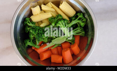 Mix di vegetali di carota, broccoli e baby corn disposti secondo i colori in una ciotola di metallo. Foto Stock