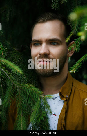 Giovani carino elegante ragazzo sogni nel verde e lussureggiante rami di abete su un giorno di estate Foto Stock