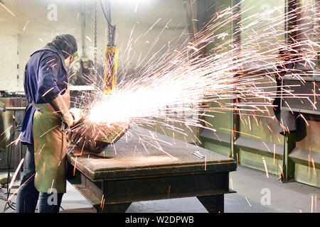 I lavoratori di attrezzature di protezione in un lavoro di fonderia su un pezzo fuso con una macchina di macinazione sul posto di lavoro Foto Stock