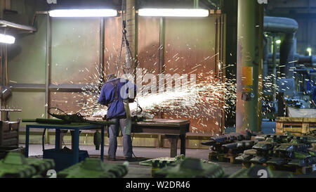 I lavoratori di attrezzature di protezione in un lavoro di fonderia su un pezzo fuso con una macchina di macinazione sul posto di lavoro Foto Stock