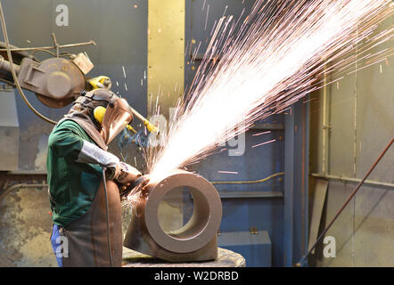 I lavoratori di attrezzature di protezione in un lavoro di fonderia su un pezzo fuso con una macchina di macinazione sul posto di lavoro Foto Stock