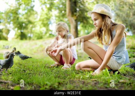 Due graziosi piccole sorelle alimentazione di uccelli sul giorno di estate. Alimentazione bambini piccioni e anatre all'esterno. Tempo libero attivo con i bambini Foto Stock