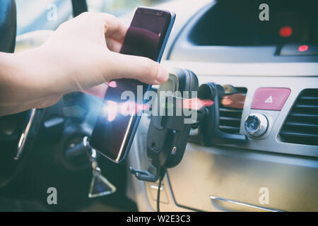 Moderno smartphone wireless di ricarica in auto con una mano mettendo un telefono su di esso. Cruscotto in background. Foto Stock