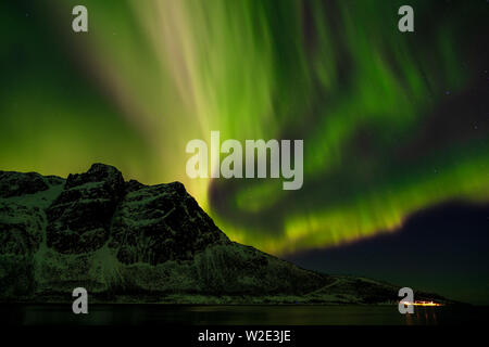 Pesante luce verde settentrionale su montagna innevata Ramnafjellet in inverno, Troms, Norvegia Foto Stock