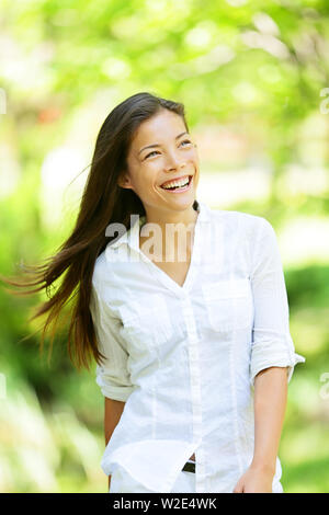 Gioioso vivace donna in primavera o estate park la trasmissione via IR di un ampio sorriso mentre cammina lungo la gioia nella freschezza della natura e la luce calda del sole attraverso le foglie degli alberi verdi Foto Stock