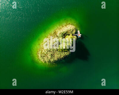 Antenna vista dall'alto in basso di una piccola isola. Birds Eye view di splendidi e verdi acque del lago di Gela circondato da foreste di pini. Le nuvole riflettono in Gela la Foto Stock