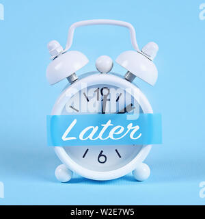 La procrastinazione, ritardo e concetto di urgenza. White orologio sveglia con una nota adesiva con il testo più tardi. Foto Stock