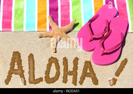 Hawaii spiaggia concetto di viaggio. ALOHA testo scritto in sabbia con acqua accanto al telo da spiaggia e sandali estivi e stelle marine. Vacanza alle Hawaii vacanze sfondo. Foto Stock