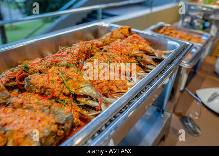 Un cibo tailandese agitare il pesce fritto in una salsa piccante in alluminio piastra triangolare sulla linea buffet nella parte anteriore della sala per seminari. Foto Stock