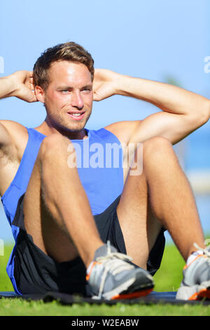 L'uomo facendo sit ups all'aperto. Maschio modello fitness training di sedersi esercizio durante il fuori allenamento in erba in estate. Bel maschio muscolare modello dello sport lavoro fuori. Foto Stock