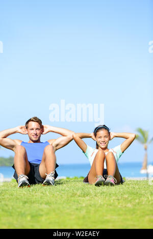 Persone che esercitano - Giovane facendo sit ups all'esterno. Coppia Fitness facendo esercizio situps durante al di fuori della formazione trasversale di allenamento. Felice giovane coppia multirazziale, donna asiatica, uomo caucasico. Foto Stock