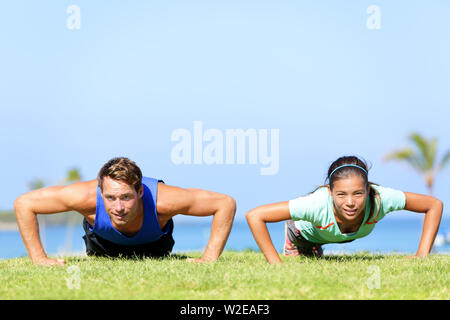 Sport fitness giovane facendo ups push all'aperto. I giovani atleti facendo pushups esercizio al di fuori di erba in estate. Uomo caucasico modello sport e donna asiatica fitness facendo modello push-up allenamento. Foto Stock