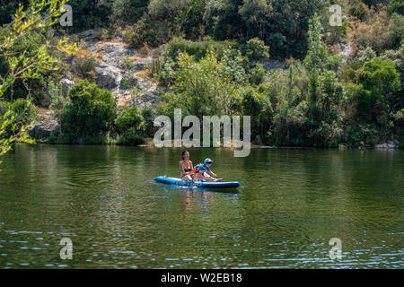 Giovane madre insegnare un ragazzino come utilizzare una racchetta di bordo su un lago Foto Stock