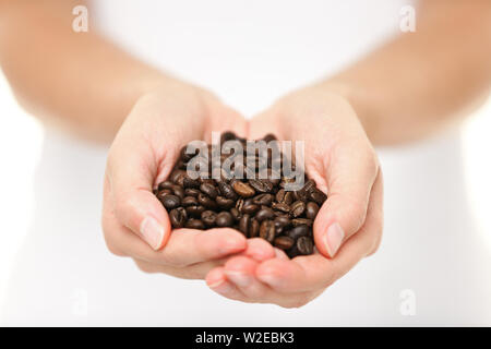 Chicchi di caffè - donna mostra di medie chicchi di caffè tostati manciata. Close up della donna che mantiene i chicchi di caffè in mani. Foto Stock