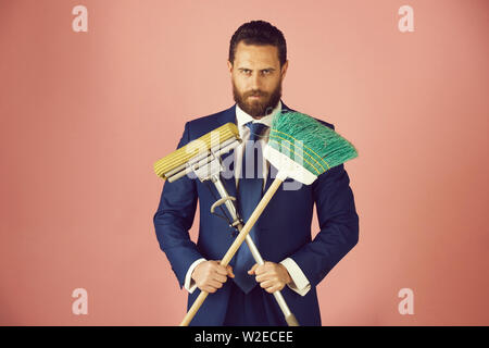 Bel giovane imprenditore con la scopa di pulizia su sfondo rosa. Foto Stock