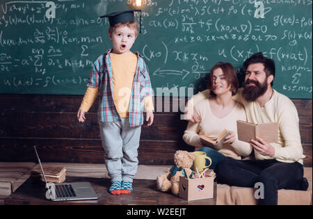 I genitori in ascolto il loro figlio, controllo errori con prenota lavagna sullo sfondo. Preparazione per l'esame del concetto. Ragazzo presentando la sua conoscenza a mamma e Foto Stock