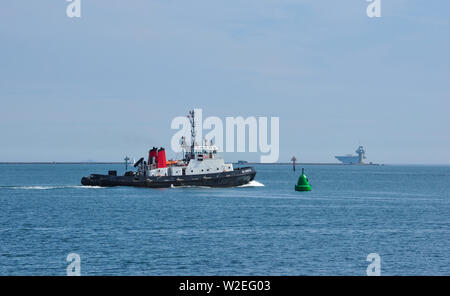 Unità gemelle Trattore rimorchiatore, SD attenta, in Plymouth Sound con portaerei HMS Queen Elizabeth oltre il frangiflutti, Devon, Inghilterra, Regno Unito Foto Stock