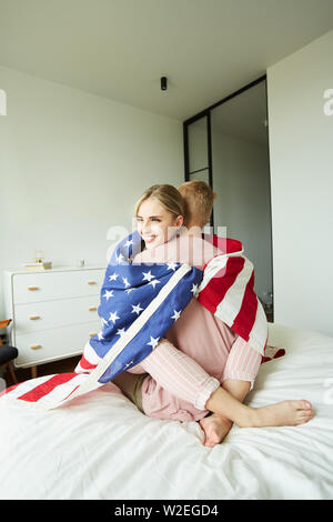 Giovani affettuoso marito e moglie seduta sul letto di abbracciare avvolto nella Bandiera americana Foto Stock