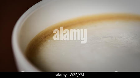Vista macro del cappuccino con la panna e la luce morbida e sfondo marrone Foto Stock