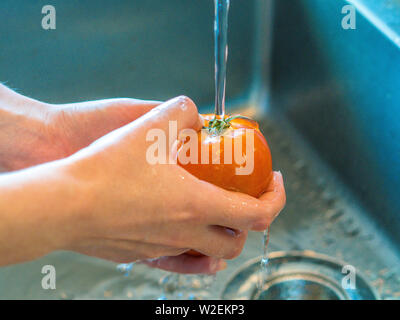 Ragazza caucasica le mani di pomodori di lavaggio sotto acqua di rubinetto nella sua cucina Foto Stock