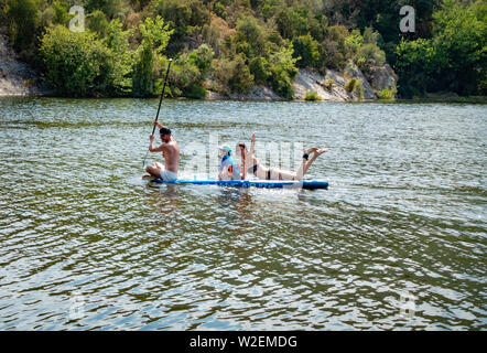 L'uomo prendendo una signora e un ragazzino su una racchetta Board viaggio su un lago Foto Stock