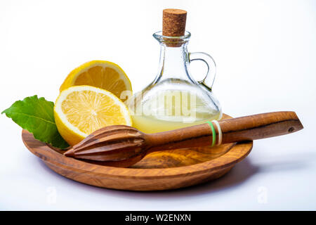 Succo di limone fresco fatto da Giallo maturo limoni siciliano utilizzato per la cottura in una bottiglia di vetro su legno d'ulivo piastra isolata su sfondo bianco Foto Stock