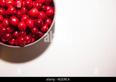 Ciotola di ciliegie su uno sfondo bianco. Ciliege rosse. Ciotola posta sulla parte superiore sinistra del telaio Foto Stock