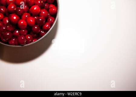 Ciotola di ciliegie su uno sfondo bianco. Ciliege rosse. Ciotola posta sulla parte superiore sinistra del telaio Foto Stock