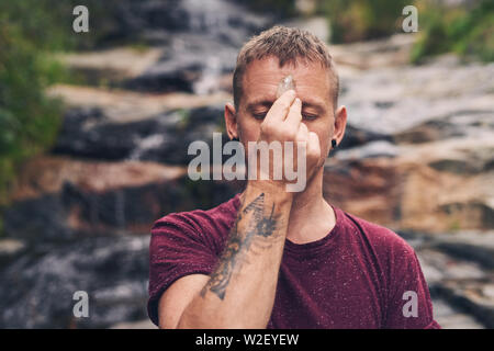 Uomo in piedi da una cascata di concentrare sul suo crystal Foto Stock