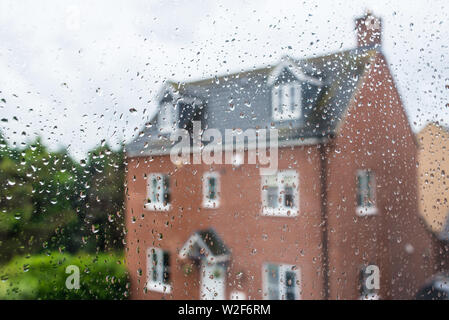 Distaccate red casa famiglia osservata attraverso una finestra di vetro coperti in caso di pioggia di gocce di acqua Foto Stock