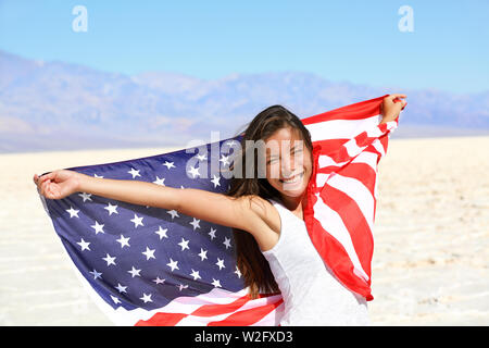 Bella e vivace patriottica giovane donna con la bandiera americana detenute nel suo mani tese in piedi in estate il sole di fronte a una distesa di sabbia bianca e montagne distanti Foto Stock