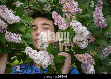 Ritratto di ragazzo adolescente in fiori lilla nel parco Foto Stock