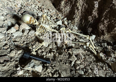 Scheletro in una grotta buia nella terra che giace sulle rocce Foto Stock