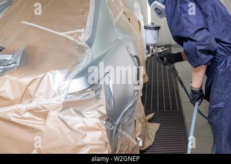 Un lavoratore di sesso maschile di vernici con una pistola a spruzzo di una parte del corpo della vettura in argento dopo essere stato danneggiato in un incidente. Parafango posteriore dal veicolo durante il rep Foto Stock