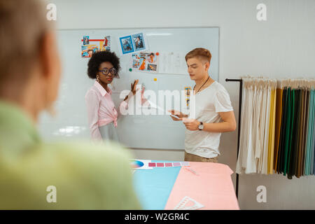 Schizzi di lavagna. Vista posteriore ritratto di una a pelo corto donna bionda guardando i bozzetti dei suoi colleghi in un fashion designer studio Foto Stock