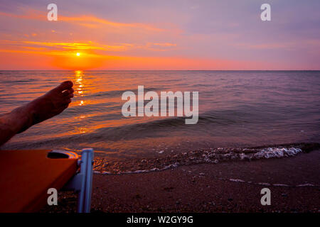L uomo per le gambe fino a quando non viene a prendere il sole in giacente spensierato in lettino accanto alla linea di costa, sulla spiaggia pubblica. Foto Stock