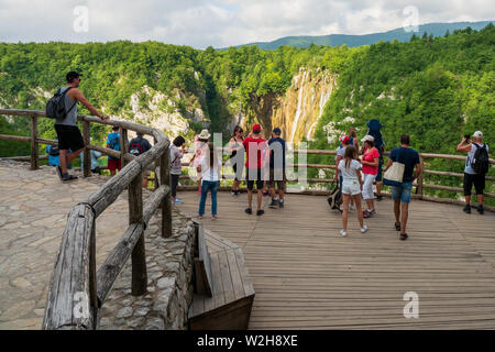 I turisti su una tavola di legno observation deck affacciato sullo splendido scenario del Parco Nazionale dei Laghi di Plitvice con il Veliki schiaffo in background Foto Stock