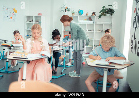 Insegnante attento ad aiutare i suoi alunni uno dopo l'altro. Foto Stock