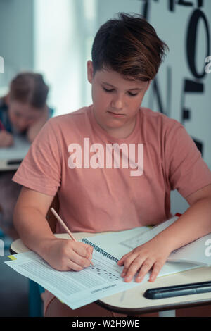 Pupilla focalizzato la scrittura del suo test in una cartella di lavoro. Foto Stock