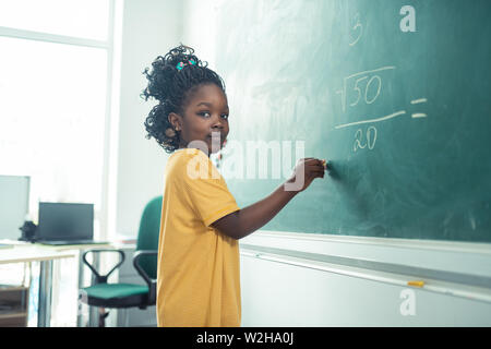 School girl pensando cosa scrivere su una lavagna. Foto Stock