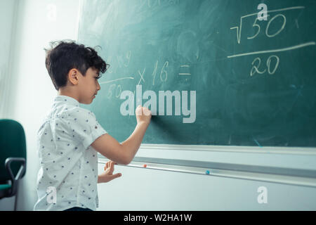 Poco concentrata schoolboy scrivere sulla lavagna. Foto Stock