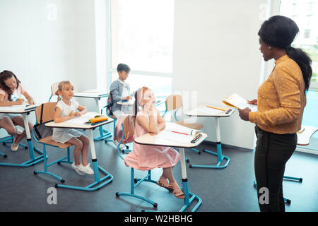 Ragazza carina in abito rosa alzando la mano mentre rispondendo alla domanda Foto Stock