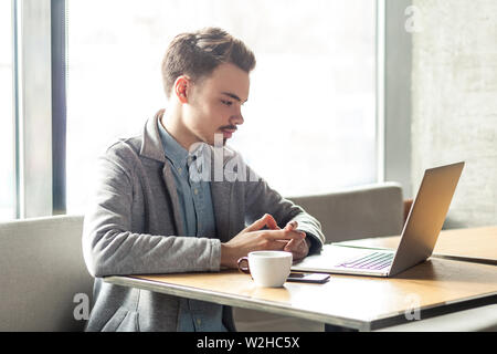 Ritratto di giovane di successo imprenditore gravi lavorando sul computer in ufficio. considerato imprenditore connessione wireless tramite computer, ho Foto Stock