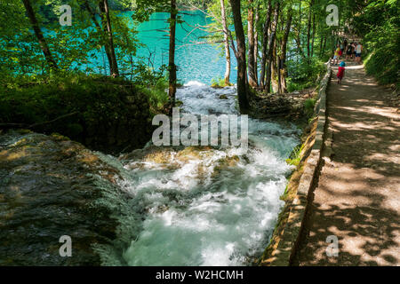 Gli escursionisti passeggiando lungo il marciapiede passando le cascate di acqua correre verso il basso in azure laghetti colorati presso il Parco Nazionale dei Laghi di Plitvice, Croazia Foto Stock