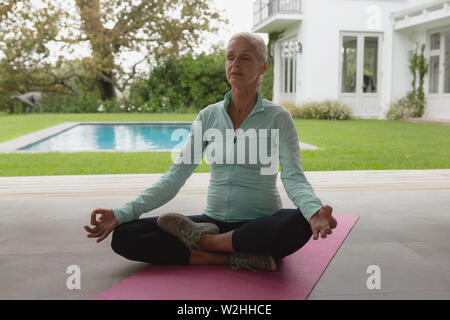 Attiva donna senior fare yoga sul tappeto di esercizio nel portico di casa Foto Stock