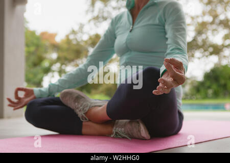 Attiva donna senior fare yoga sul tappeto di esercizio nel portico di casa Foto Stock