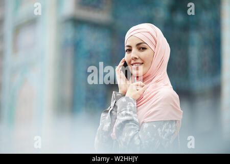 Ritratto di sorridere bellissimo centro religioso-donna orientale in rosa hijab in piedi presso la moschea e la risposta a una chiamata Foto Stock